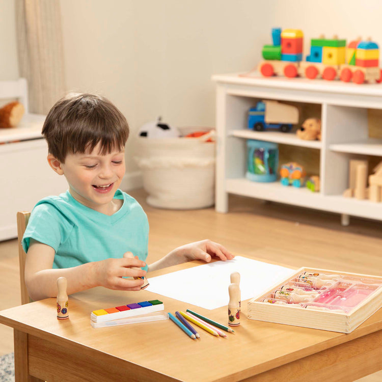 A kid playing with The Melissa & Doug Deluxe Happy Handle Stamp Set With 10 Stamps, 5 Colored Pencils, and 6-Color Washable Ink Pad