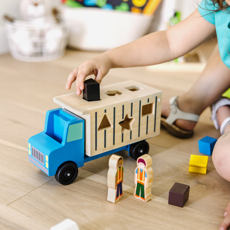 A kid playing with The Melissa & Doug Shape-Sorting Wooden Dump Truck Toy With 9 Colorful Shapes and 2 Play Figures