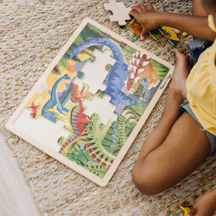 A kid playing with The Melissa & Doug Dinosaurs Wooden Jigsaw Puzzle With Storage Tray (24 pcs)