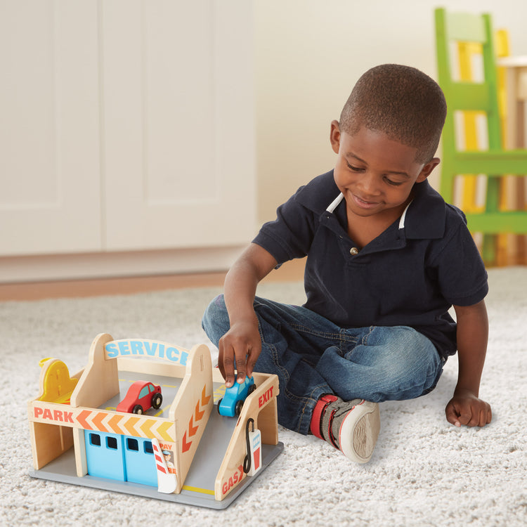 A kid playing with The Melissa & Doug Service Station Parking Garage With 2 Wooden Cars and Drive-Thru Car Wash