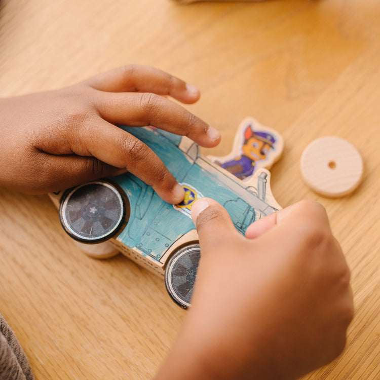 A kid playing with The Melissa & Doug PAW Patrol Wooden Vehicles Craft Kit - 3 Decorate Your Own Vehicles, 3 Play Figures