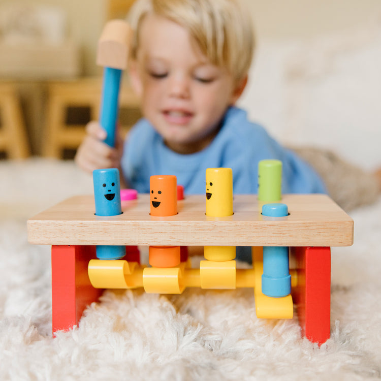 A kid playing with The Melissa & Doug Deluxe Pounding Bench Wooden Preschool Learning Toy With Mallet