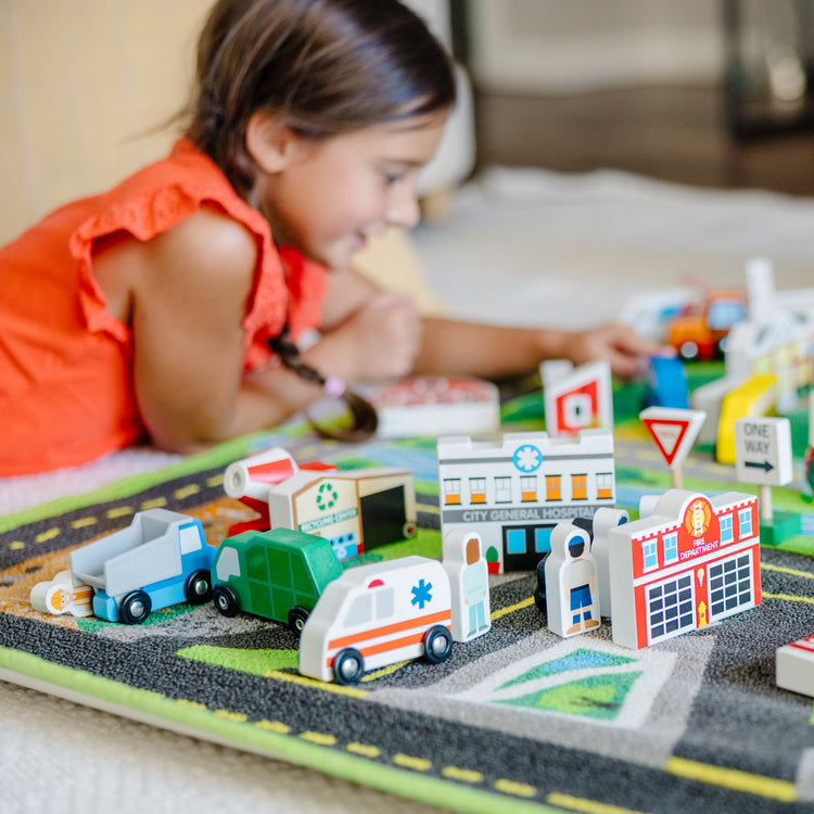 A kid playing with The Melissa & Doug Deluxe Activity Road Rug Play Set with 49 Wooden Vehicles and Play Pieces