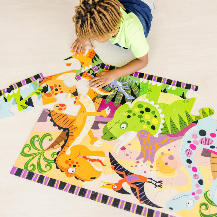 A kid playing with The Melissa & Doug Dinosaur Dawn Jumbo Jigsaw Floor Puzzle (24 pcs, 2 x 3 feet)