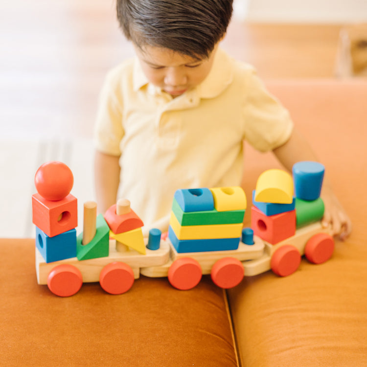 A kid playing with The Melissa & Doug Wooden Stacking Train Learning Toy Vehicle With 18 Connecting Pcs