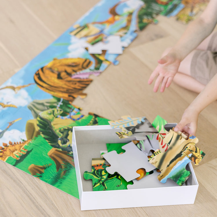 A kid playing with The Melissa & Doug Land of Dinosaurs Floor Puzzle (48 pcs, 4 feet long)