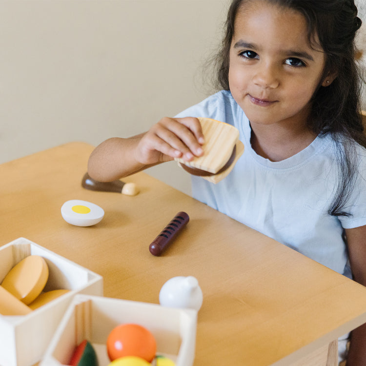 A kid playing with The Melissa & Doug Food Groups - 21 Wooden Pieces and 4 Crates, Multi