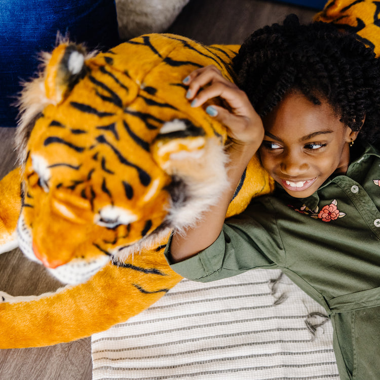 A kid playing with The Melissa & Doug Giant Tiger - Lifelike Stuffed Animal, Over 5 Feet Long (Includes Tail)