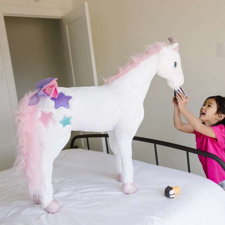 A kid playing with The Melissa & Doug Giant Unicorn - Lifelike Plush Stuffed Animal (over 2 feet tall)