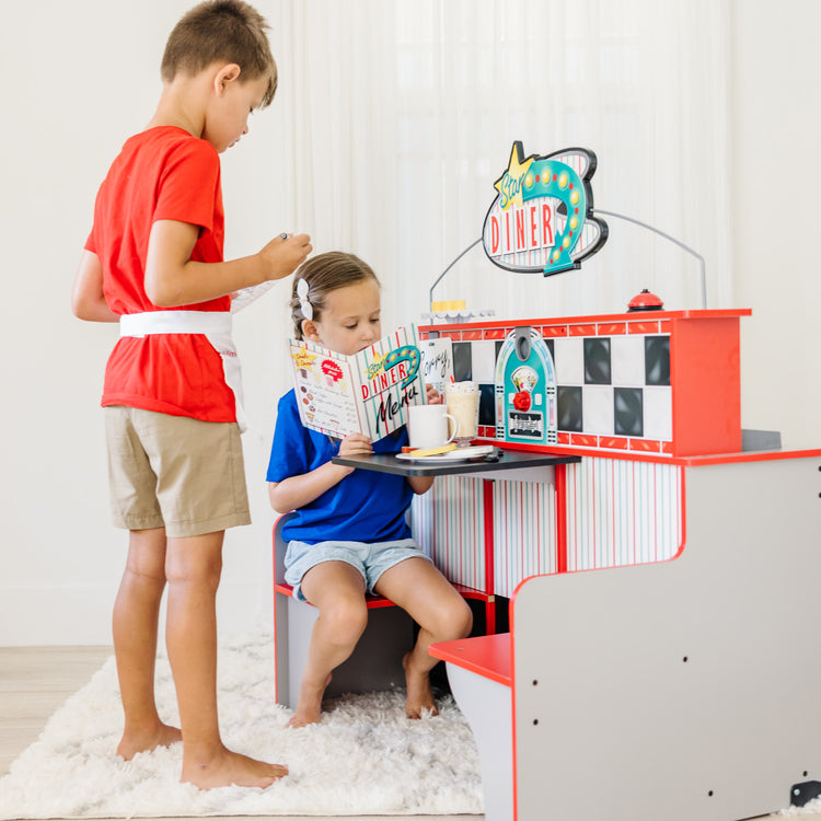 A kid playing with The Melissa & Doug Double-Sided Wooden Star Diner Restaurant Play Space