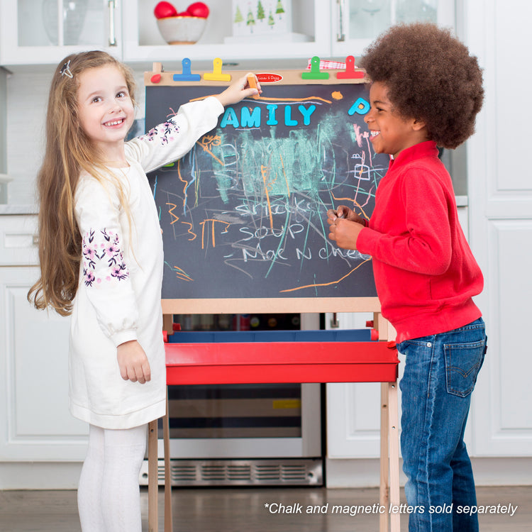 A kid playing with The Melissa & Doug Deluxe Magnetic Standing Art Easel With Chalkboard, Dry-Erase Board, and 39 Letter and Number Magnets