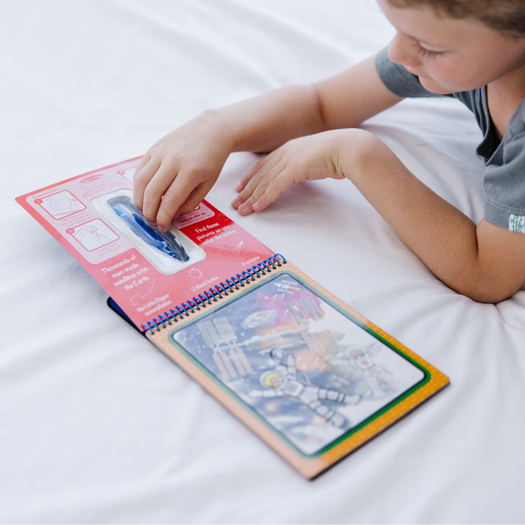 A kid playing with The Melissa & Doug On the Go Space Water Wow! Reusable Mess-Free Water-Reveal Activity Pad