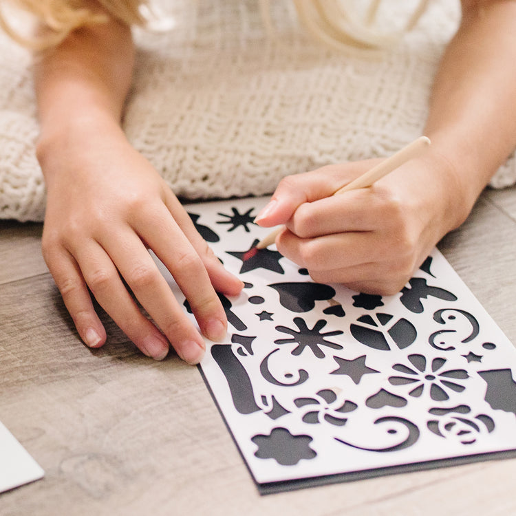 A kid playing with The Melissa & Doug Deluxe Combo Scratch Art Set: 16 Boards, 2 Stylus Tools, 3 Frames