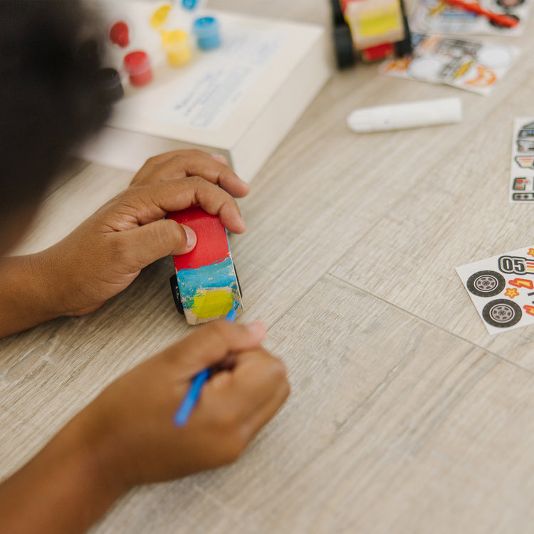 A kid playing with The Melissa & Doug Decorate-Your-Own Wooden Craft Kits Set - Race Car and Monster Truck