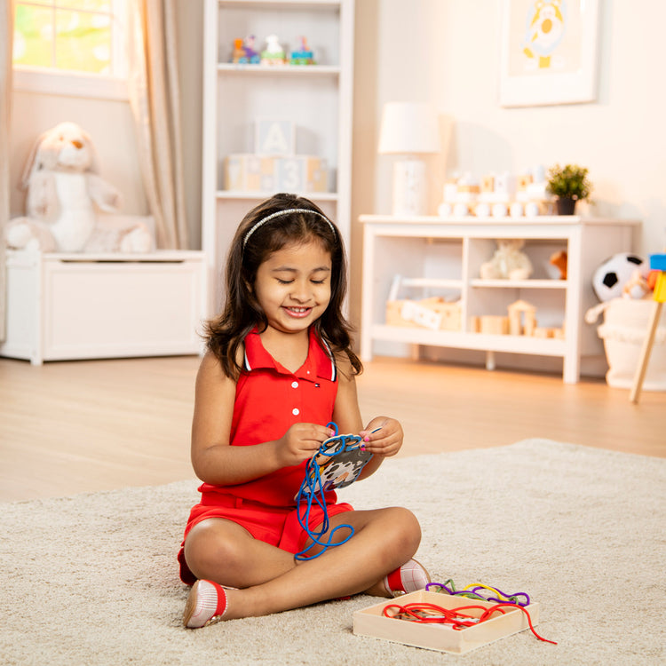 A kid playing with The Melissa & Doug Lace and Trace Activity Set: 5 Wooden Panels and 5 Matching Laces - Farm