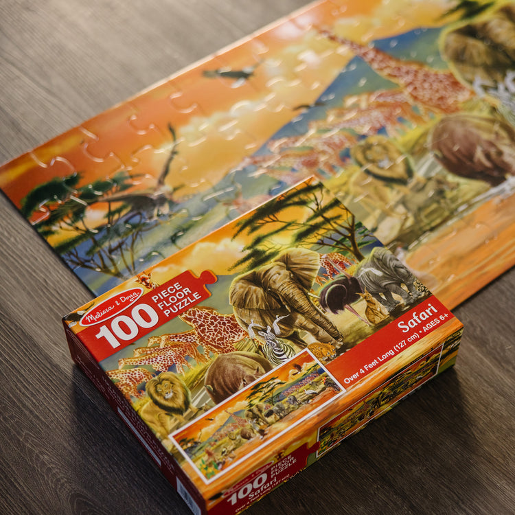 A kid playing with The Melissa & Doug African Plains Safari Jumbo Jigsaw Floor Puzzle (100 pcs, over 4 feet long)