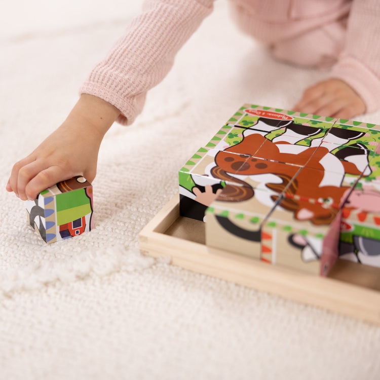 A kid playing with The Melissa & Doug Farm Wooden Cube Puzzle With Storage Tray - 6 Puzzles in 1 (16 pcs)