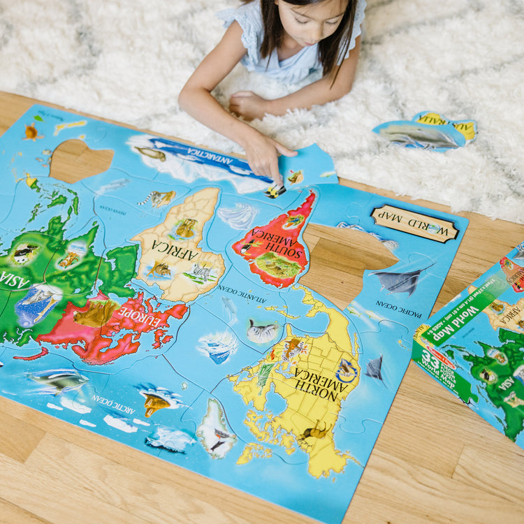 A kid playing with The Melissa & Doug World Map Jumbo Jigsaw Floor Puzzle (33 pcs, 2 x 3 feet)