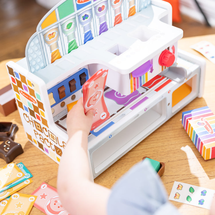 A kid playing with The Melissa & Doug Wooden Chocolate Factory Pretend Play Set, Play Food Candy Maker for Boys and Girls