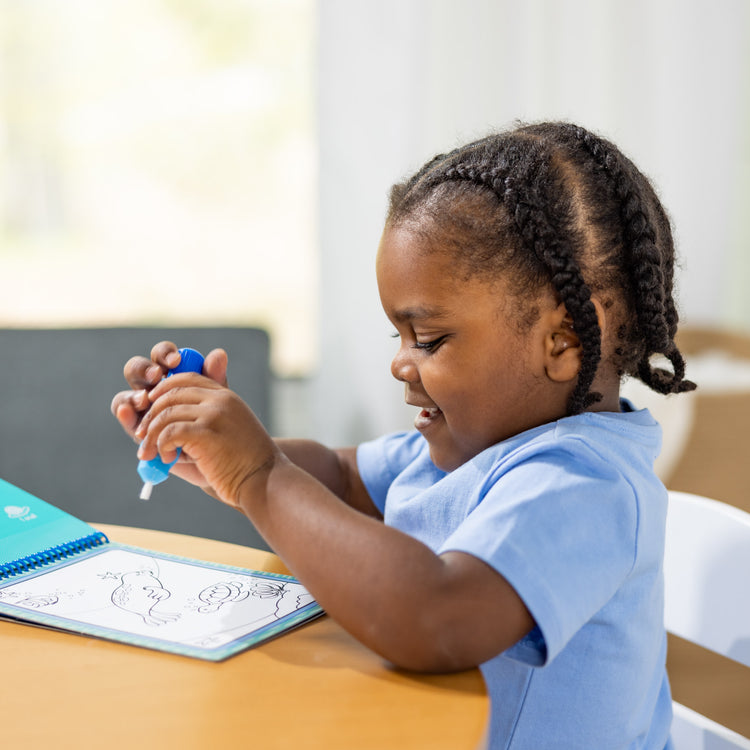 A kid playing with The Melissa & Doug On the Go Water Wow! Reusable Water-Reveal Activity Pad - Under the Sea