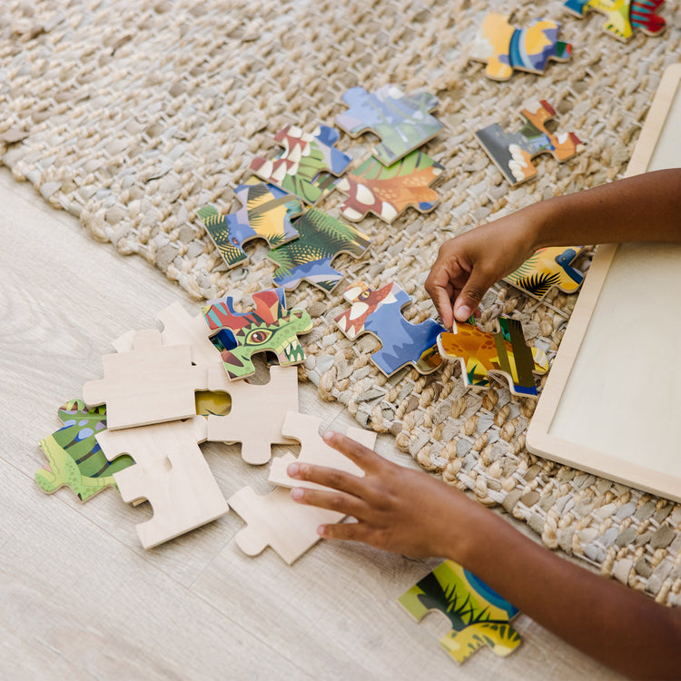 A kid playing with The Melissa & Doug Dinosaurs Wooden Jigsaw Puzzle With Storage Tray (24 pcs)