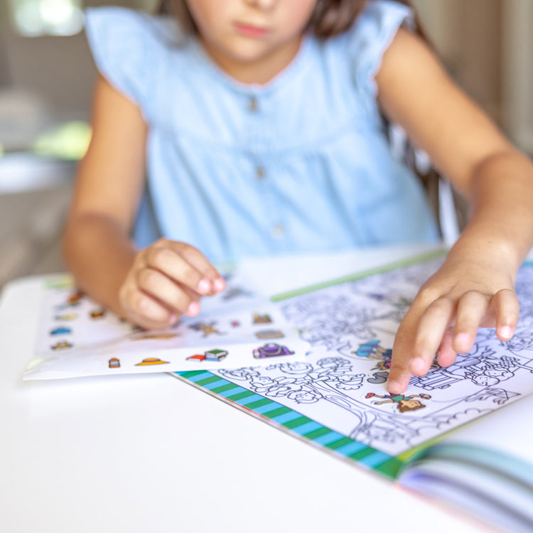 A kid playing with The Melissa & Doug Seek and Find Sticker Pad – Around Town (400+ Stickers, 14 Scenes to Color)