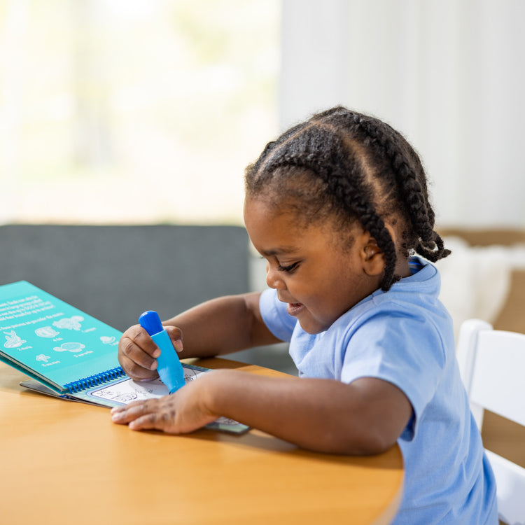 A kid playing with The Melissa & Doug On the Go Water Wow! Reusable Water-Reveal Activity Pad - Under the Sea