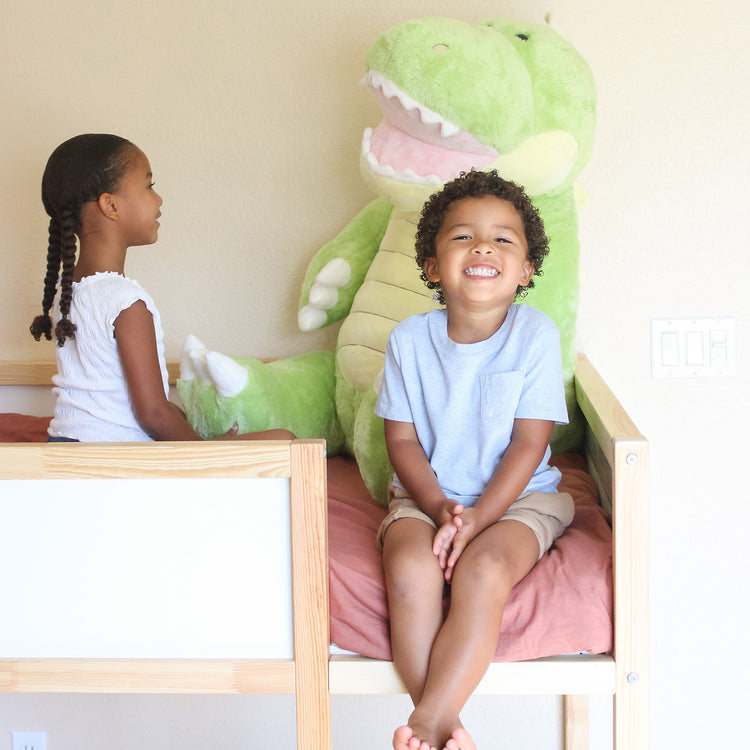 A kid playing with The Melissa & Doug Gentle Jumbos Dinosaur Giant Stuffed Plush Animal (Sits Nearly 3 Feet Tall)