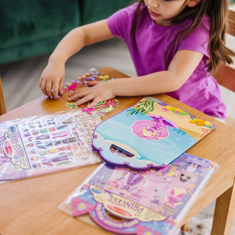 A kid playing with The Melissa & Doug Puffy Sticker Activity Books Set: Dress-Up, Princess, Mermaid - 208 Reusable Stickers