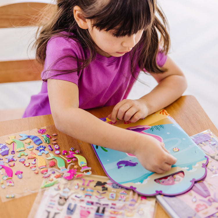 A kid playing with The Melissa & Doug Puffy Sticker Activity Books Set: Dress-Up, Princess, Mermaid - 208 Reusable Stickers