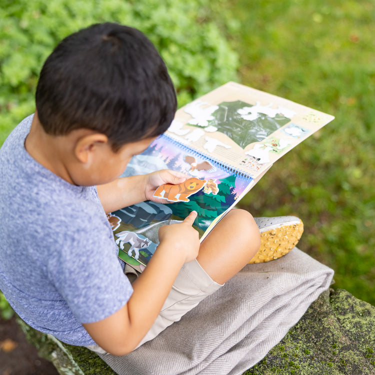 A kid playing with The Melissa & Doug National Parks Reusable Stickers Jumbo Pad: Park Animals - 5 Scenes, 121 Puffy and Cling Stickers