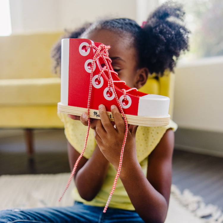 A kid playing with The Melissa & Doug Deluxe Wood Lacing Sneaker - Learn to Tie a Shoe Educational Toy