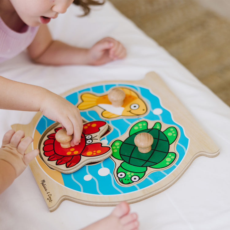 A kid playing with The Melissa & Doug Animals Jumbo Knob Wooden Puzzles Set - Fish and Pets