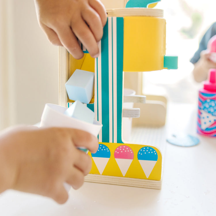 A kid playing with The Melissa & Doug Fun at the Fair! Wooden Snow-Cone and Slushie Play Food Set