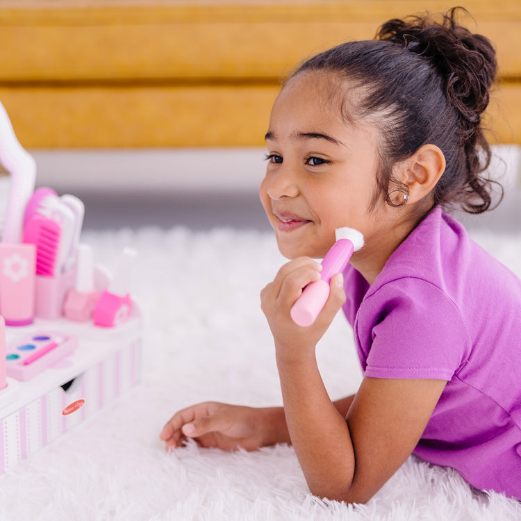 A kid playing with The Melissa & Doug Wooden Beauty Salon Play Set With Vanity and Accessories (18 pcs)