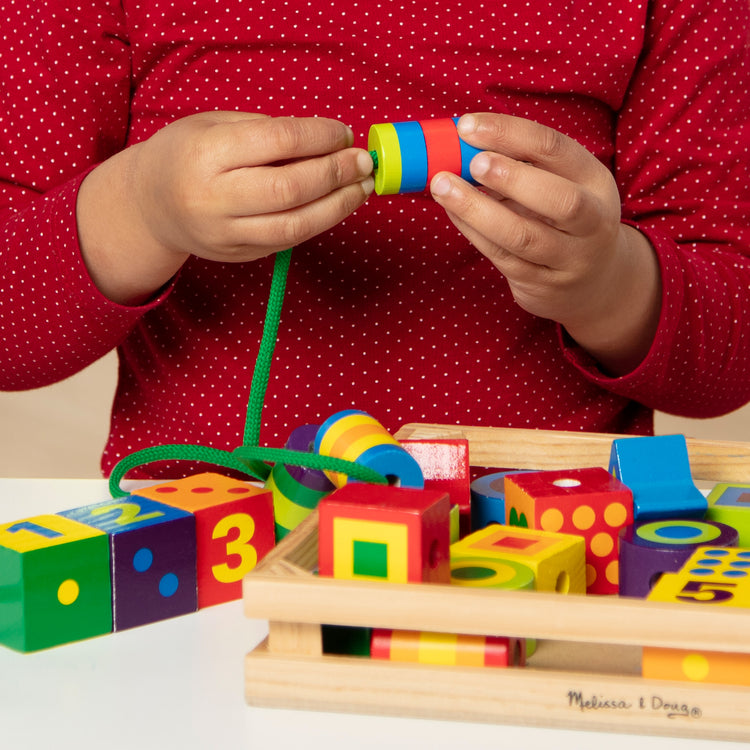 A kid playing with The Melissa & Doug Deluxe Wooden Lacing Beads - Educational Activity With 27 Beads and 2 Laces