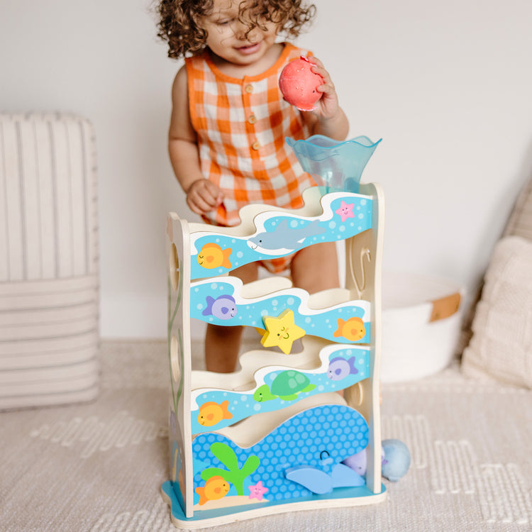 A kid playing with The Melissa & Doug Rollables Wooden Ocean Slide Infant and Toddler Toy (5 Pieces)