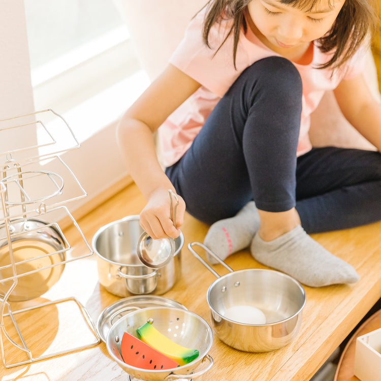 A kid playing with The Melissa & Doug Stainless Steel Pots and Pans Pretend Play Kitchen Set for Kids (8 pcs)