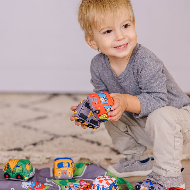 A kid playing with The Melissa & Doug Take-Along Town Play Mat (19.25 x 14.25 inches) With 9 Soft Vehicles