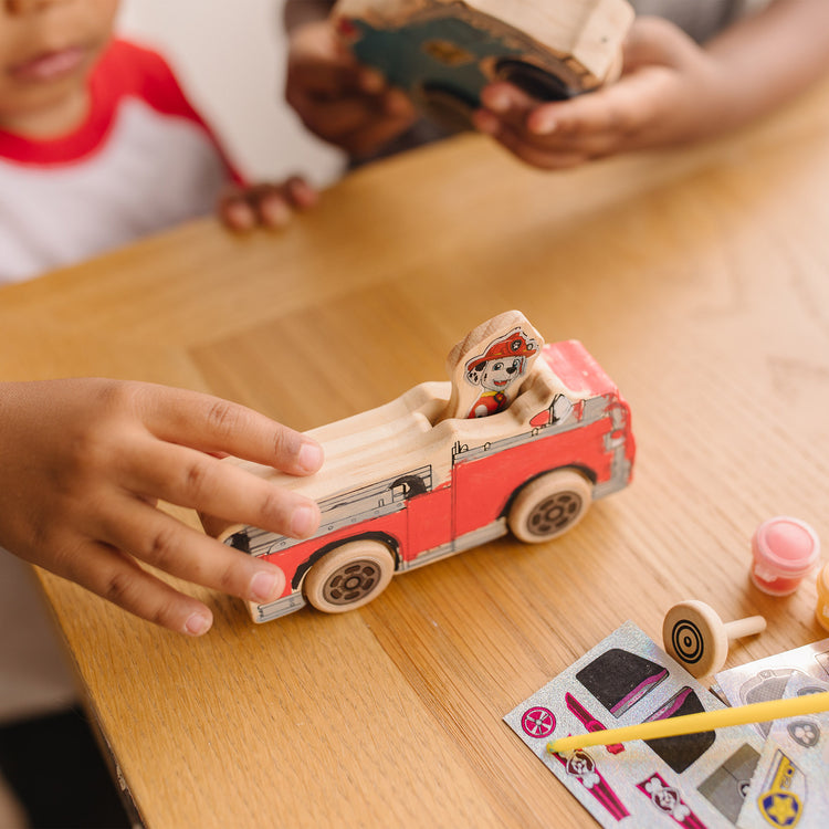 A kid playing with The Melissa & Doug PAW Patrol Wooden Vehicles Craft Kit - 3 Decorate Your Own Vehicles, 3 Play Figures