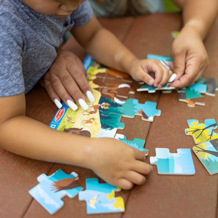 A kid playing with The Melissa & Doug Yellowstone National Park Wooden Jigsaw Puzzle – 24 Pieces, Animal and Plant ID Guide