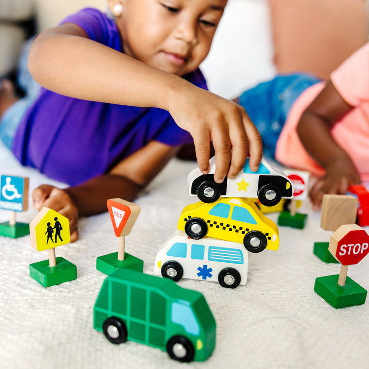 A kid playing with The Melissa & Doug Wooden Vehicles and Traffic Signs With 6 Cars and 9 Signs