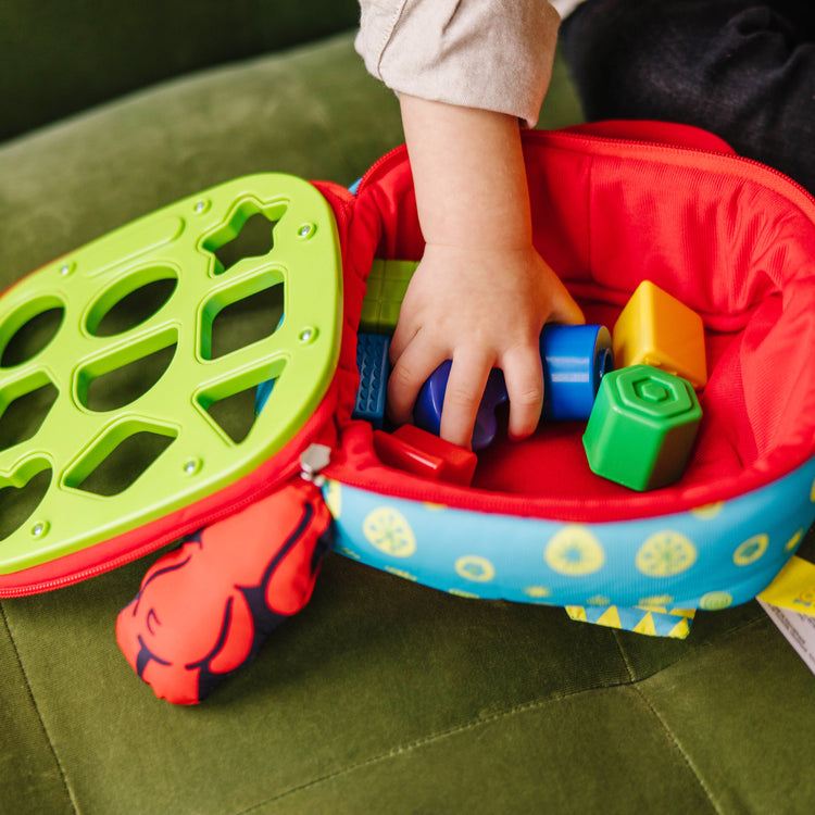 A kid playing with The Melissa & Doug K's Kids Take-Along Shape Sorter Baby Toy With 2-Sided Activity Bag and 9 Textured Shape Blocks