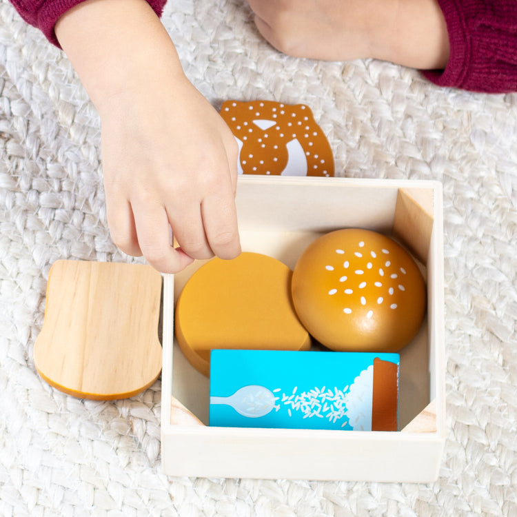 A kid playing with The Melissa & Doug Wooden Food Groups Play Food Set – Grains