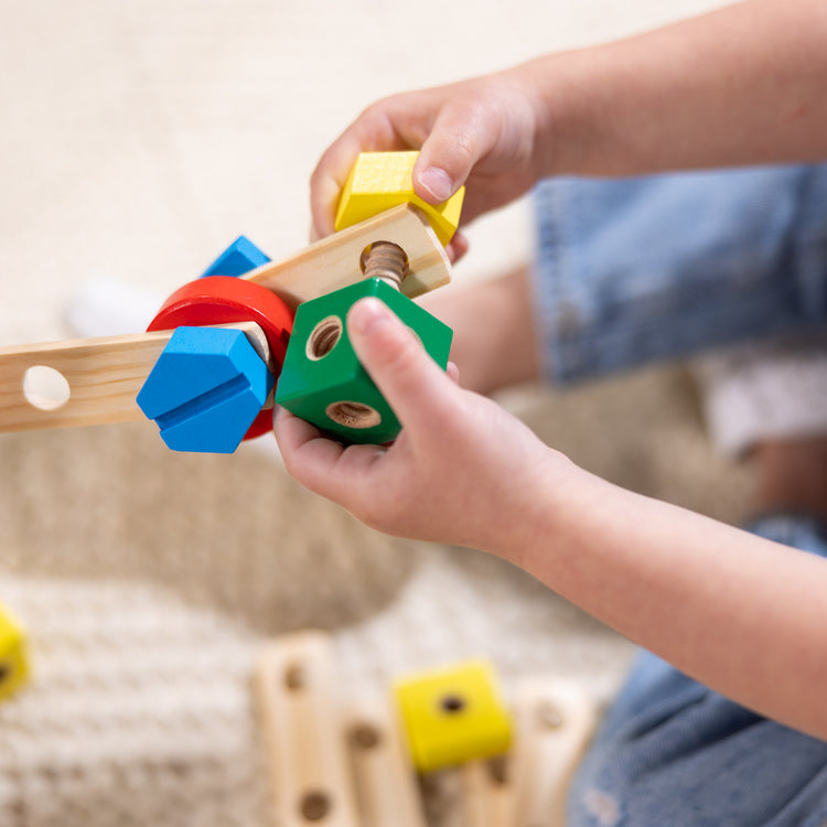 A kid playing with The Melissa & Doug Wooden Construction Building Toy Play Set in a Box, Developmental Educational Toy (48 pcs)