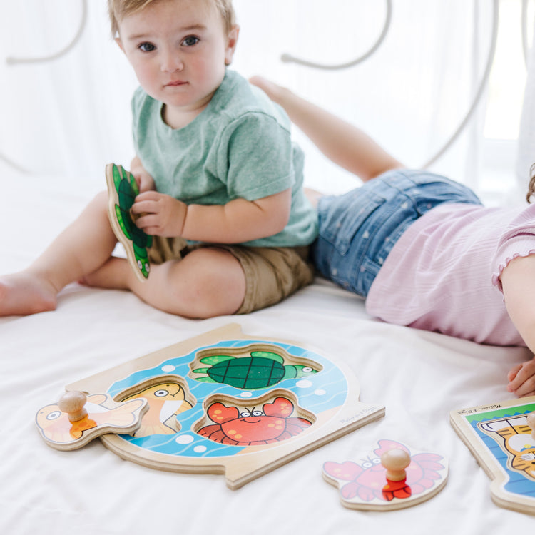 A kid playing with The Melissa & Doug Animals Jumbo Knob Wooden Puzzles Set - Fish and Pets