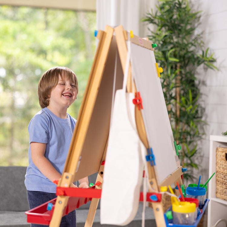 A kid playing with The Melissa & Doug Deluxe Standing Art Easel - Dry-Erase Board, Chalkboard, Paper Roller