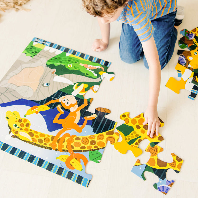 A kid playing with The Melissa & Doug Safari Social Jumbo Jigsaw Floor Puzzle (24 pcs, 2 x 3 feet)