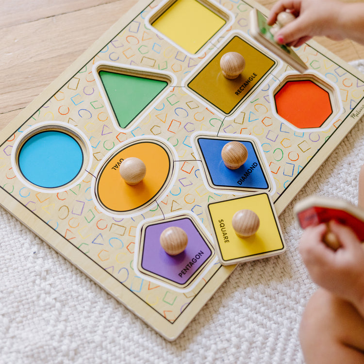 A kid playing with The Melissa & Doug Deluxe Jumbo Knob Wooden Puzzle - Geometric Shapes (8 pcs)