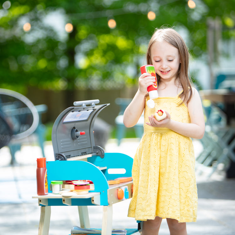 A kid playing with The Melissa & Doug Wooden Deluxe Barbecue Grill, Smoker and Pizza Oven Play Food Toy for Pretend Play Cooking for Kids